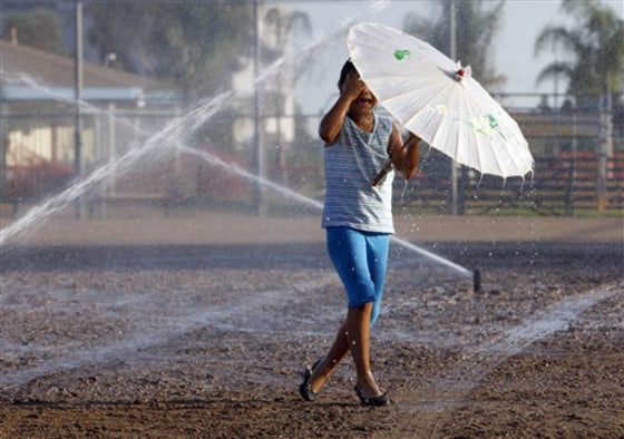 A girl plays in the sprinklers to beat the heat in Monterey Park, Calif. on Monday. Southern California Edison says more than 27,000 of its customers were without power Tuesday morning, mainly in Orange and Los Angeles counties.